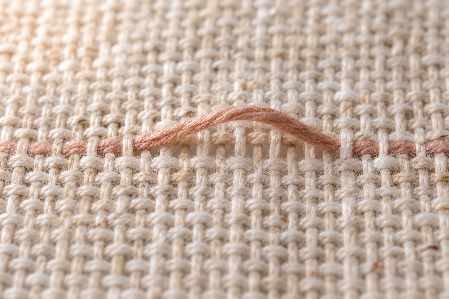 A clay-coloured thread lifted from a close weave of natural linen.
